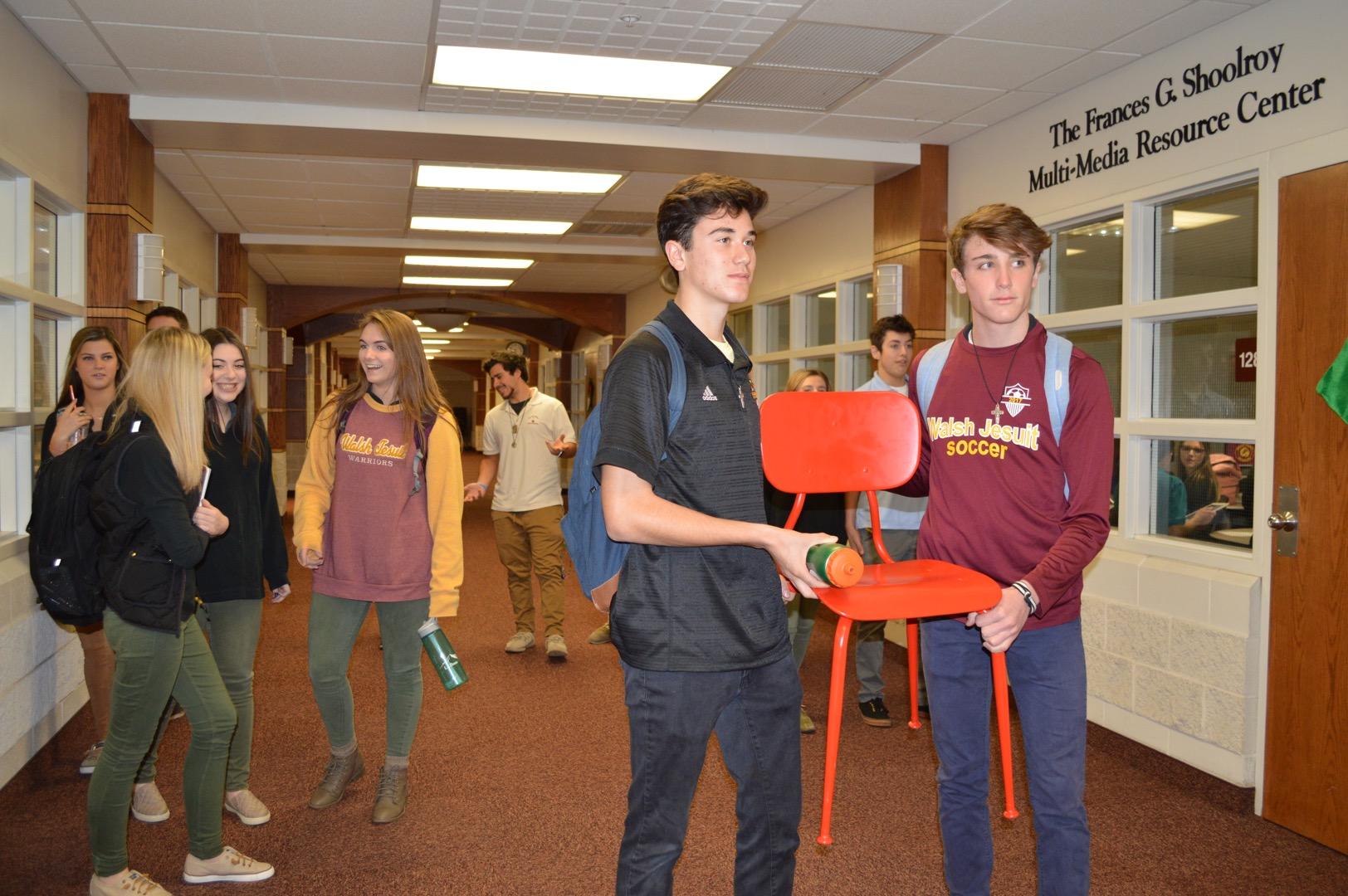 Seniors Roman Gioglio and Nico Clarke carry the Red Chair to their next class through a busy hallway. 