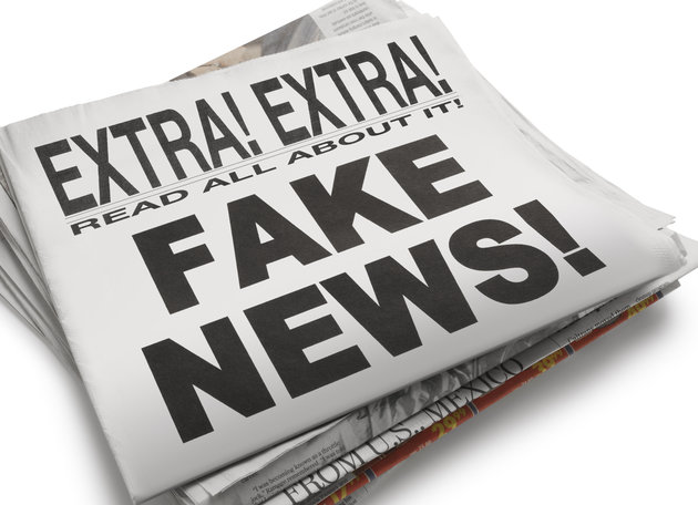 The front page of a newspaper with the headline Fake News which illustrates the current phenomena. Front section of newspaper is on top of loosely stacked remainder of newspaper. All visible text is authored by the photographer. Photographed in a studio setting on a white background with a slight wide angle lens.