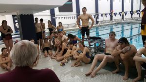 Coach Wally Lutkus leads the team in an end of practice meeting. In these meetings the coach reviews the practices and calls out specific swimmers to recognize their hard work in practice. Afterward, Coach Lutkus shouts, “Walsh on three! One, two, three!” and the team proclaims its Warrior pride, “Walsh!”