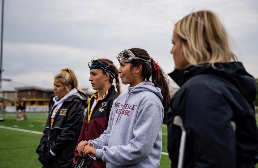 Head Coach Ms. Hudec, far right, meets with the team on the field before a game time. 