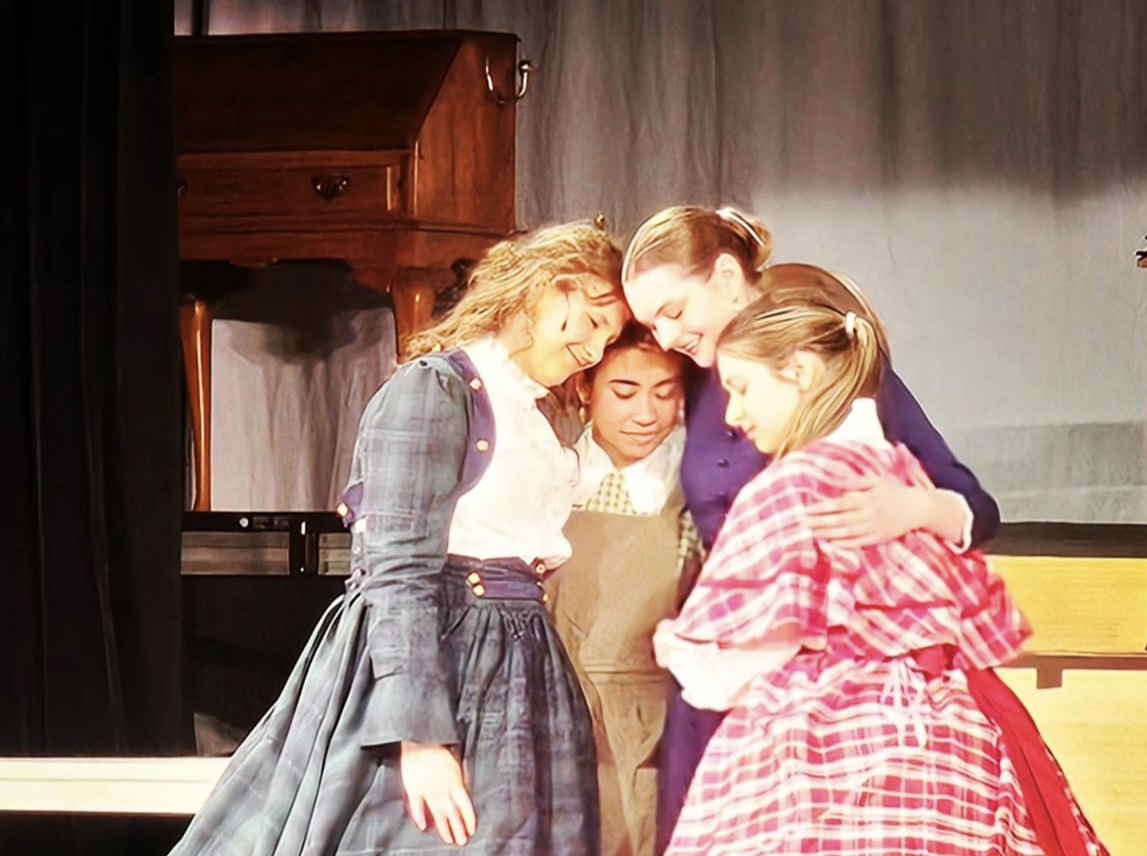 Three of the March and their mother, Marmee, embrace each other at a dress rehearsal. 